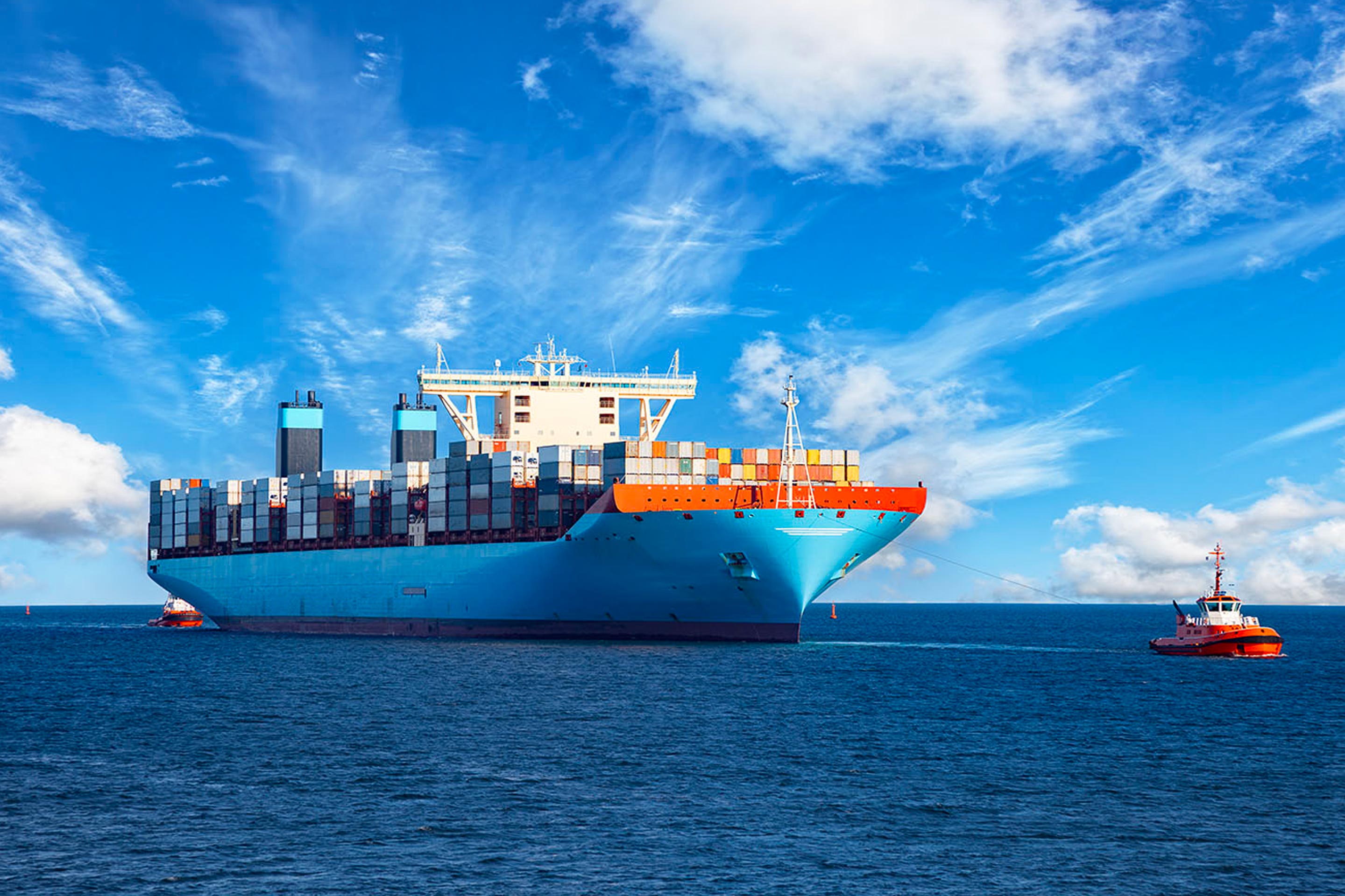 A container ship at sea, towed by tug boats