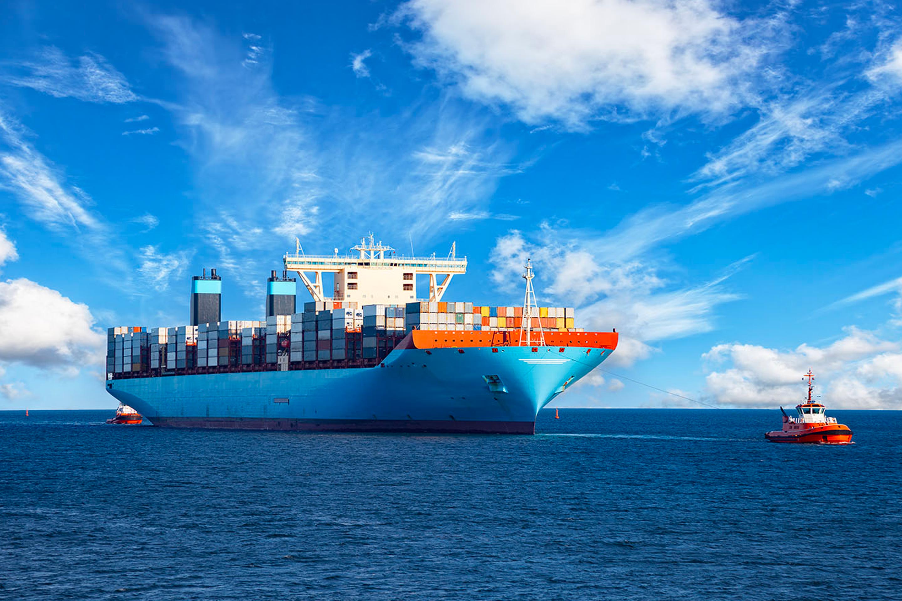 A container ship at sea, towed by tug boats
